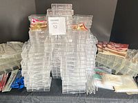 Stack of 7 large and numerous small clear plastic bead organizers with compartment dividers, shown on a table