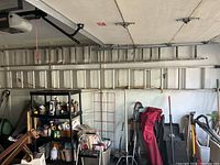 Full view of the aluminum extension ladder hanging horizontally on a garage wall with various other tools and items below it.