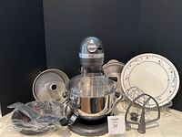 Mixer, bowl guard, three attachments, aluminum tube pan and ceramic platter arranged together