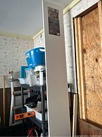 Photo of one melamine shelf standing vertically in a garage with some wear visible on edges, showing pre-drilled holes along the length.
