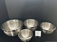 Four stainless steel mixing bowls nested and arranged in a row on a black surface.