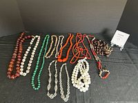 Photo of various beaded necklaces spread out on black cloth background with small numbered tag.