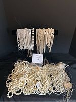 Wide view of multiple strands of white beads in mother of pearl, howlite, and faux pearls displayed on a black background and surface