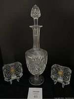 Photo of vintage crystal decanter and two square Made in England crystal ashtrays on black background.