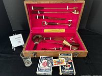 Full view of the vintage Frank Jewellers bar set including bar utensils, shot glass, and two decks of playing cards inside the original wooden case with red velvet lining.