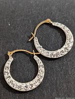 Close-up of pair of 10K gold hoop earrings with clear cubic zirconia stones on white metal face and gold backs, set on black background.