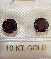 Close-up photo of pair of round garnet stud earrings mounted in 10K gold prong settings on a display card marked '10 KT. GOLD'