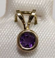 Close-up photo of round faceted purple amethyst set in 14K yellow gold pendant with bail.