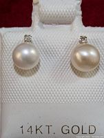 Pair of pearl and diamond stud earrings shown on display card marked 14KT Gold against red background.