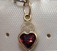 Close-up of heart-shaped red garnet set in 14K gold with gold swirl detail above the stone.