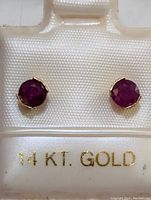 Clear close up of ruby earrings set in 14K gold with '14 KT. GOLD' label visible.