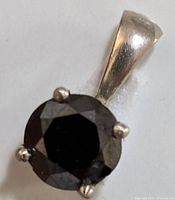 Close-up photo showing the front face of the pendant with round black diamond held in four gold prongs.