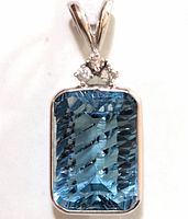 Close-up photo of pendant showing large rectangular blue topaz and three small diamond cluster on top, set in 14K white gold.