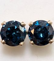 Close-up front view of round brilliant-cut blue diamond stud earrings in 14K yellow gold four-prong settings