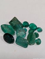 Eleven loose emerald gemstones on white background, various shapes and sizes