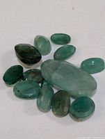 Loose emerald gemstones displayed with variety in shape and size, oval and marquise cuts, visible inclusions, shades of green.