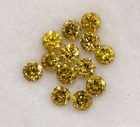 Close-up of multiple lab grown yellow diamonds on a white surface, showing sharp facets and bright yellow color.