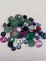 Mixed loose gemstones in various colors and cuts, displayed on white background.