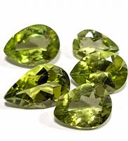 Close-up of five pear-shaped faceted green peridot stones on white background