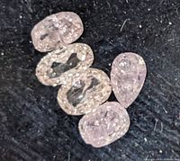 Five loose pink diamonds on a black background showing various cuts and inclusions