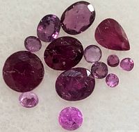 Close-up view of loose ruby gemstones showing different shapes and shades from deep red to pinkish-red with faceted cuts.