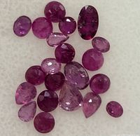 Close-up of multiple small faceted genuine rubies of various shapes and deep pink to red colors on white background.