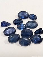 View of multiple loose blue sapphires of various sizes and cuts arranged on a white surface