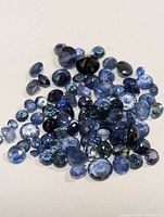 Pile of loose cut genuine sapphires in various shades of blue, oval and round shapes, faceted gemstones on white background.