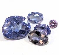 Close-up of five faceted tanzanite gemstones varying in size with visible inclusions and characteristic blue violet color, arranged on white background.