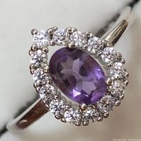 Close-up front view of ring showing oval amethyst surrounded by cubic zirconia stones in silver setting.