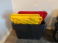 Side view of four stacked heavy duty plastic storage bins with two yellow lids and one red lid visible