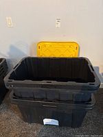 Two black heavy duty plastic storage bins stacked, one without lid showing inside.