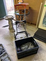 Kubota folding dolly standing behind a black plastic bin containing metal chains, placed indoors on a floor.