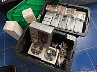 Photo showing first bin with boxed Tom Smith crackers, several packages of small colored ornaments, and coiled LED lights with remote controllers.