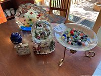 Wide view of lot items on table: glass sea life artwork, musical snow globe, hip flask, blue vial, and glass dish with marbles