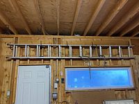 Wide view of the ladder mounted on a garage wall above a door and window, showing full length and mounting hooks.