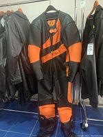 View of black and orange leather motorcycle riding suit hanging on a rack among other leather jackets.