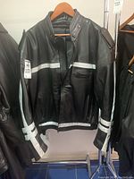 Front view of men's black leather jacket with white reflective stripes and zippered pockets hung on wooden hanger