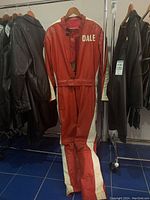 Red and white leather riding suit with 'DALE' on chest hanging on rack among other leather jackets.