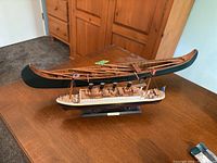 Two ship models on a table: a carved wood canoe with paddles and a wood Titanic ship model.
