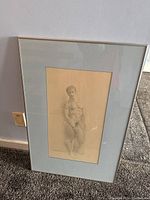 Full framed pencil drawing of a nude male figure standing, shown against wall and carpet floor.