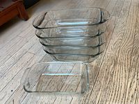 Stack of four 9-inch Anchor Hocking glass baking dishes with one 8-inch Pyrex baking dish in front on floor