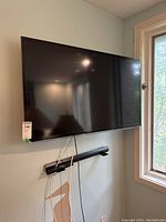 Samsung 46 inch flat screen TV mounted on wall near window with cables hanging, wall mount visible below television.