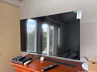 Samsung 46 inch flatscreen TV on wooden stand, with remote controls and a small white device next to it. Clear reflection visible on screen.