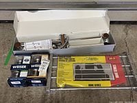 Boxed Weiser SmartKey door locks alongside WindowGuard window security bars and boxed shower head with sliding rail.