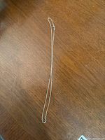 Image showing full length of the thin silver chain necklace laid flat on a wooden surface.