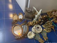 Small decorative gold and cream statues, candle holders, and two golden oval mirrors with ornate frames on blue tile floor.