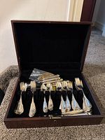 Open wooden box showing inner velvet-lined tray with arranged forks, spoons and knives
