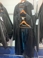 Three black leather jackets hanging on a rack, one open showing teal inner lining