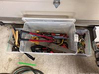 Wide view showing plastic storage bins filled with assorted hand tools including hammers, saws, crowbars, and screwdrivers.